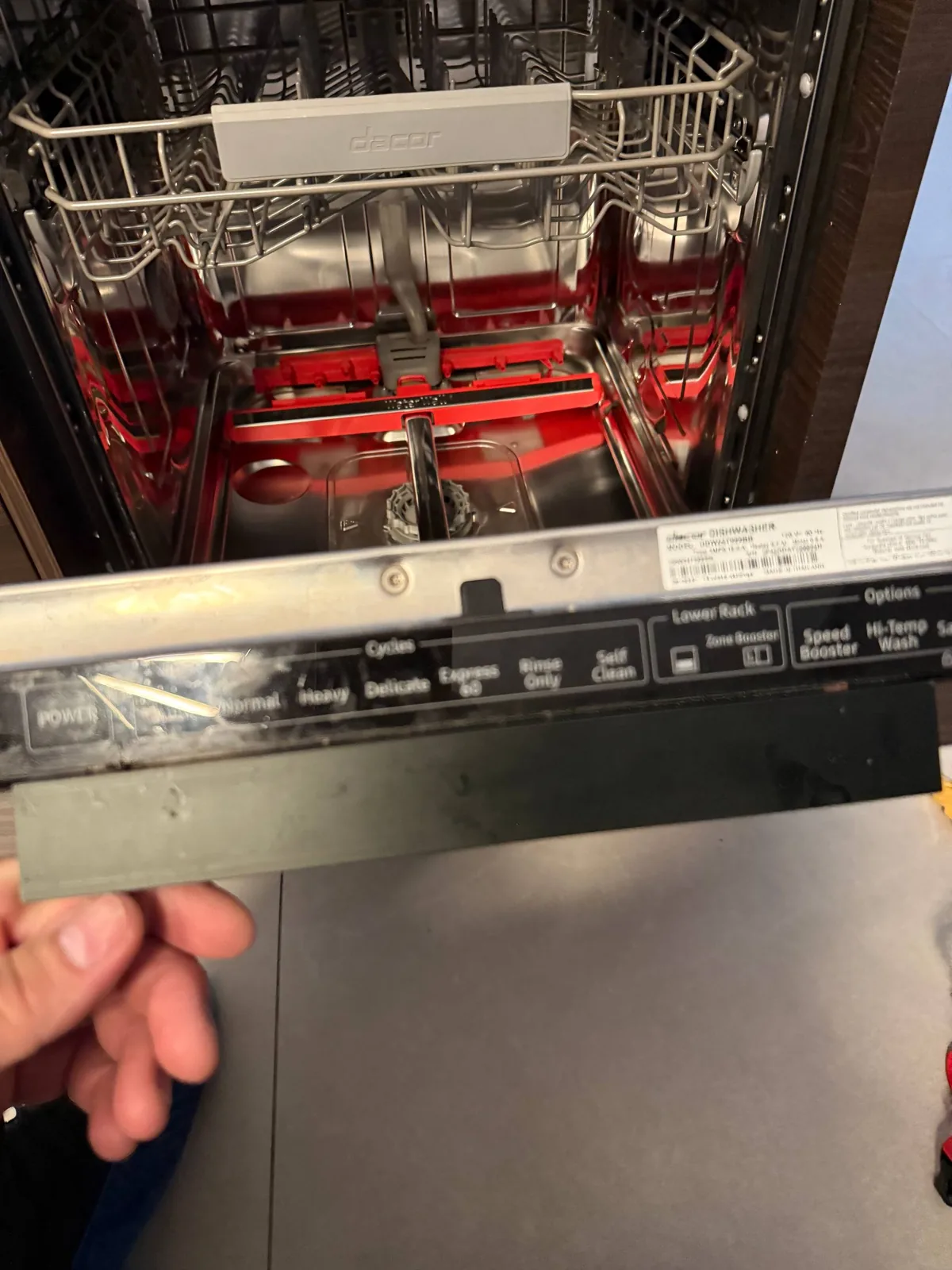 A technician working on a Dacor dishwasher, with the control panel open and the interior visible
