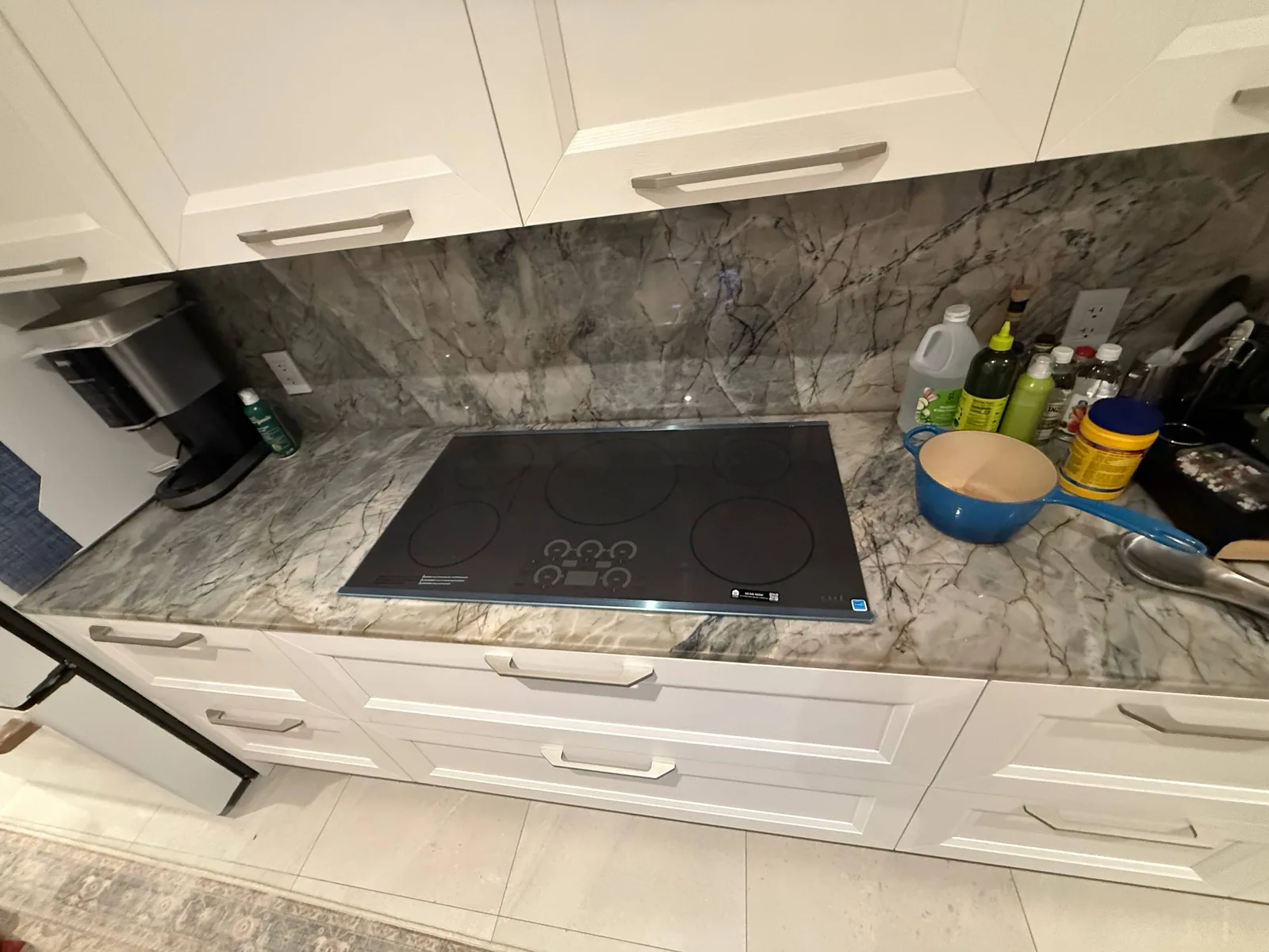 A cooktop is installed in a kitchen with white cabinets and a marble countertop