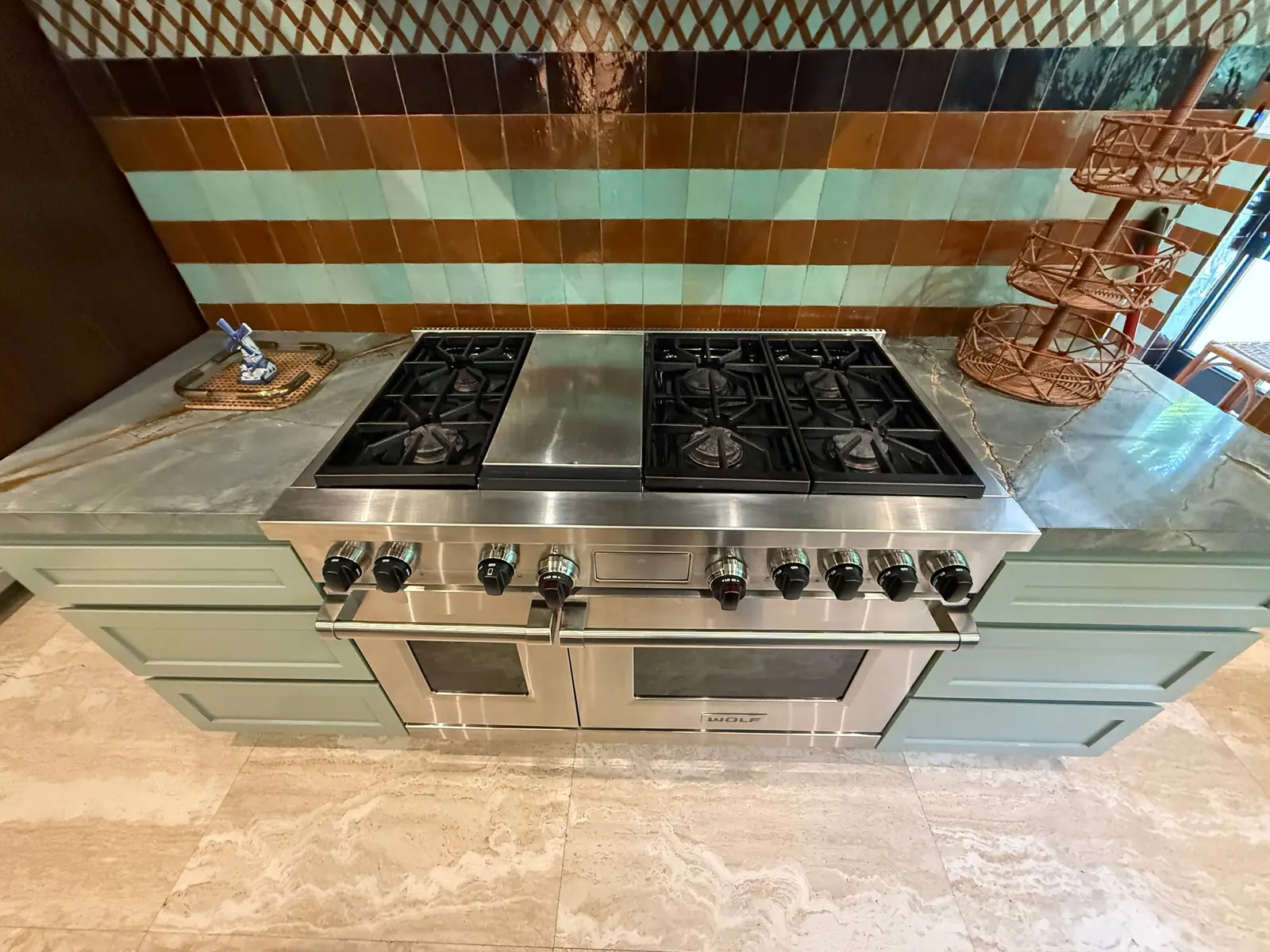 A stainless steel Wolf range and cooktop is installed in a kitchen with light blue cabinets and a patterned backsplash