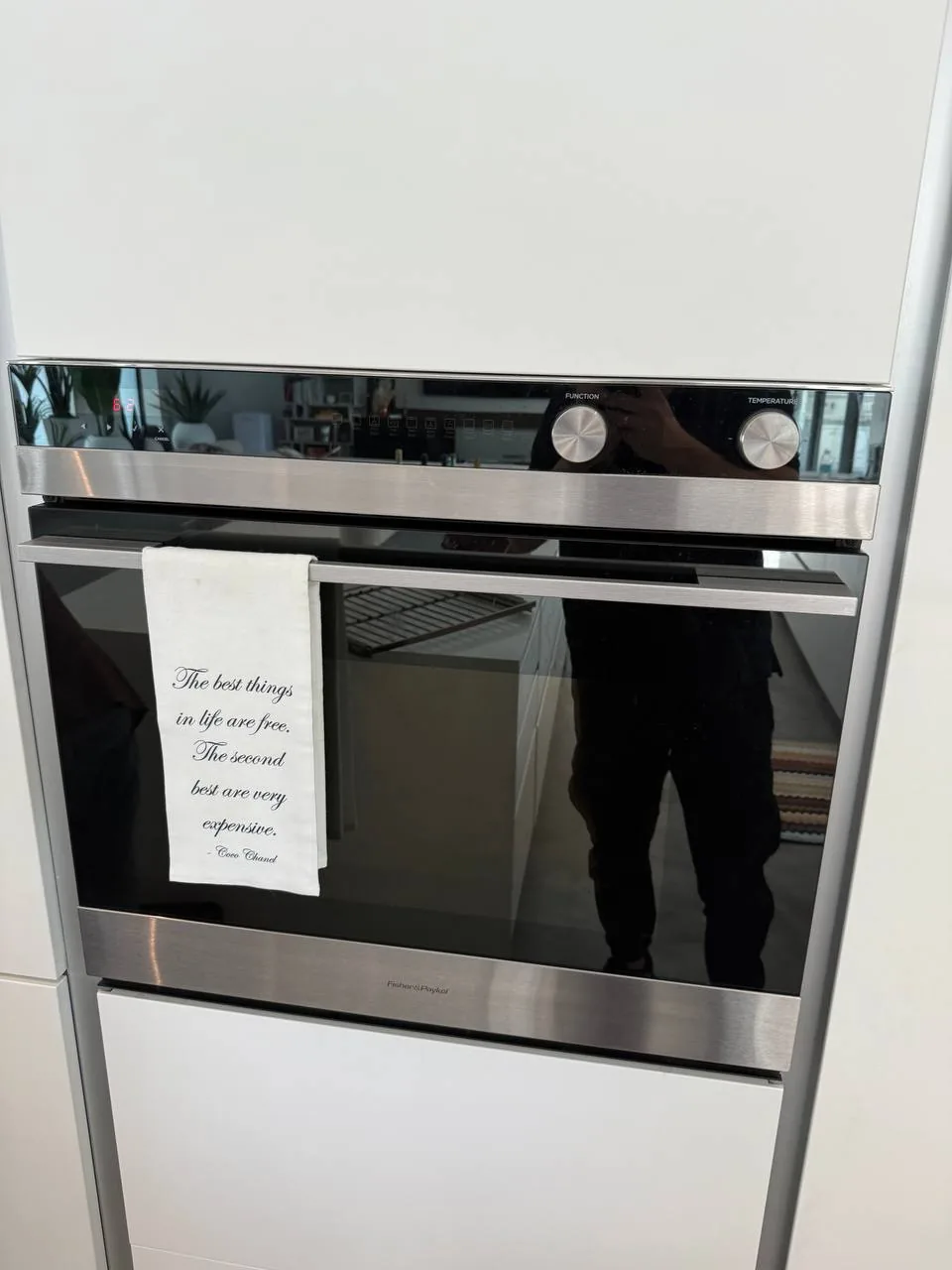A Fisher & Paykel oven with a tea towel hanging on the handle, with a person reflected in the oven door