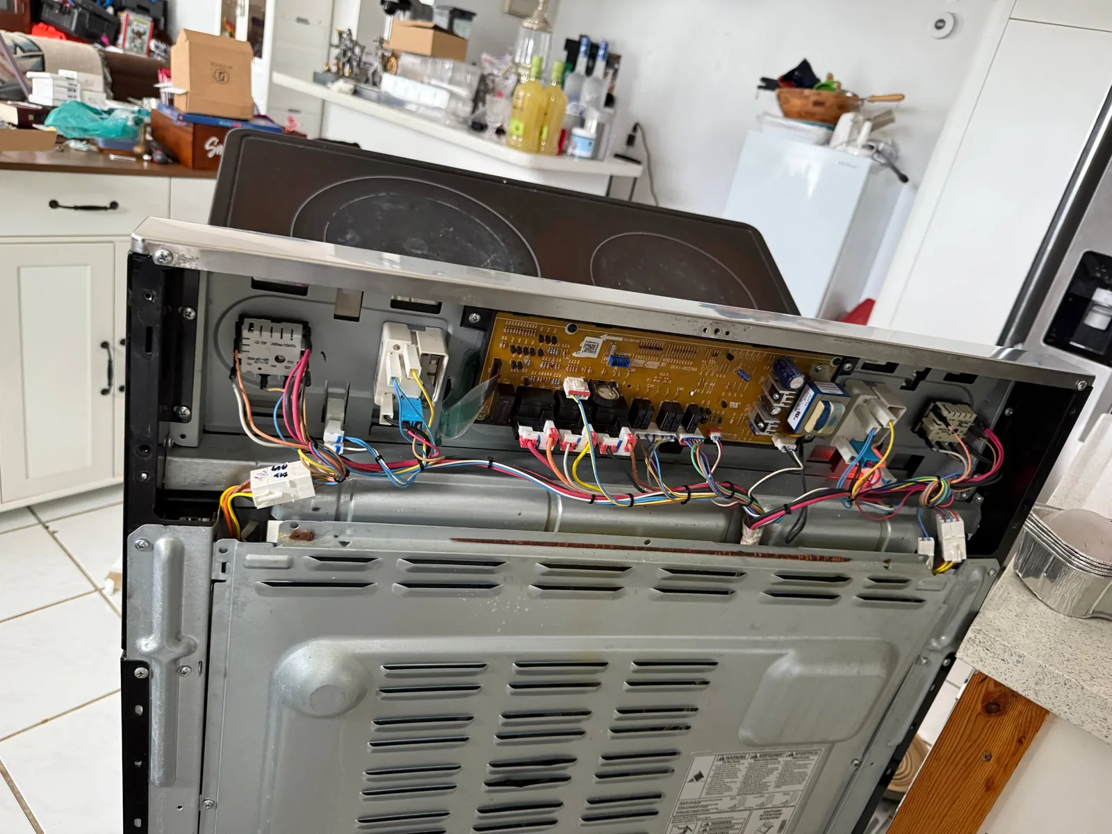 A disassembled cooktop with its internal wiring and circuit board visible in a kitchen setting