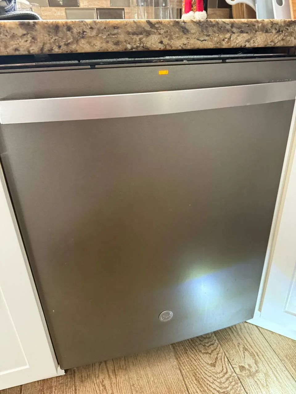 A gray GE dishwasher is installed in a kitchen with a granite countertop and white cabinets