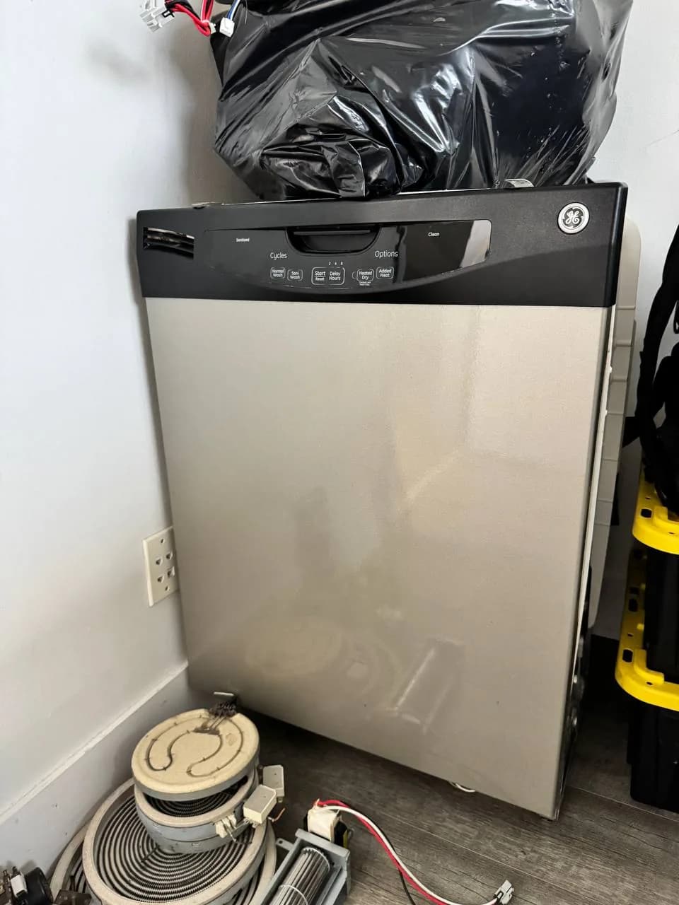 A stainless steel GE dishwasher with some removed parts on the floor