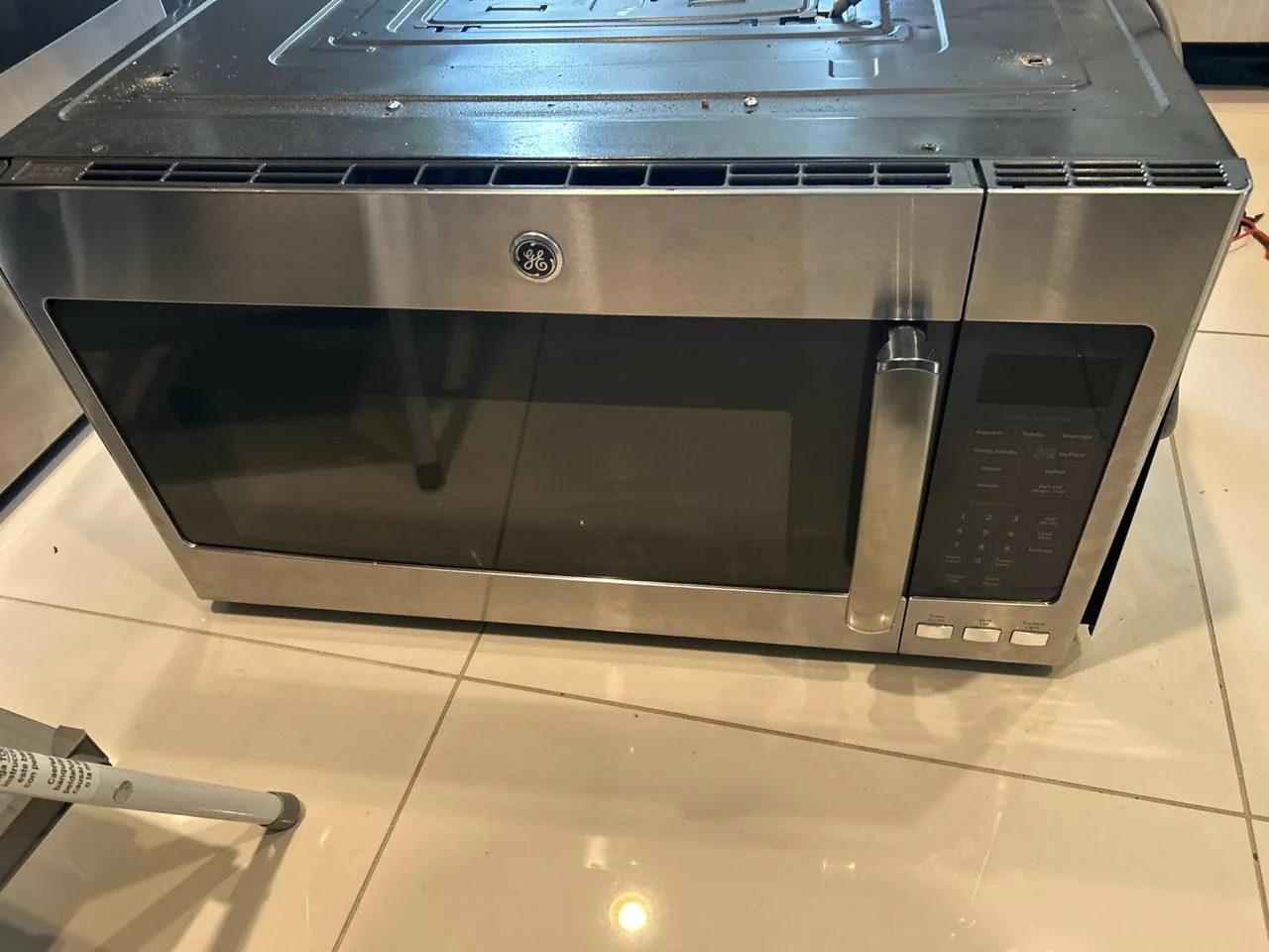 A stainless steel GE microwave is on the floor with its top panel removed for repair