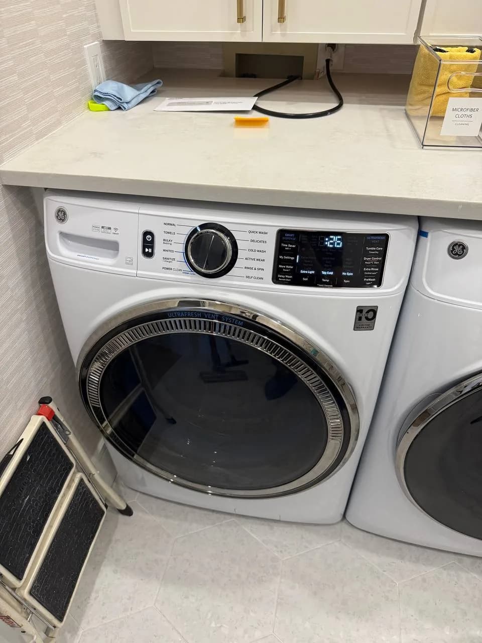 A white GE washer in a laundry room with a step stool next to it
