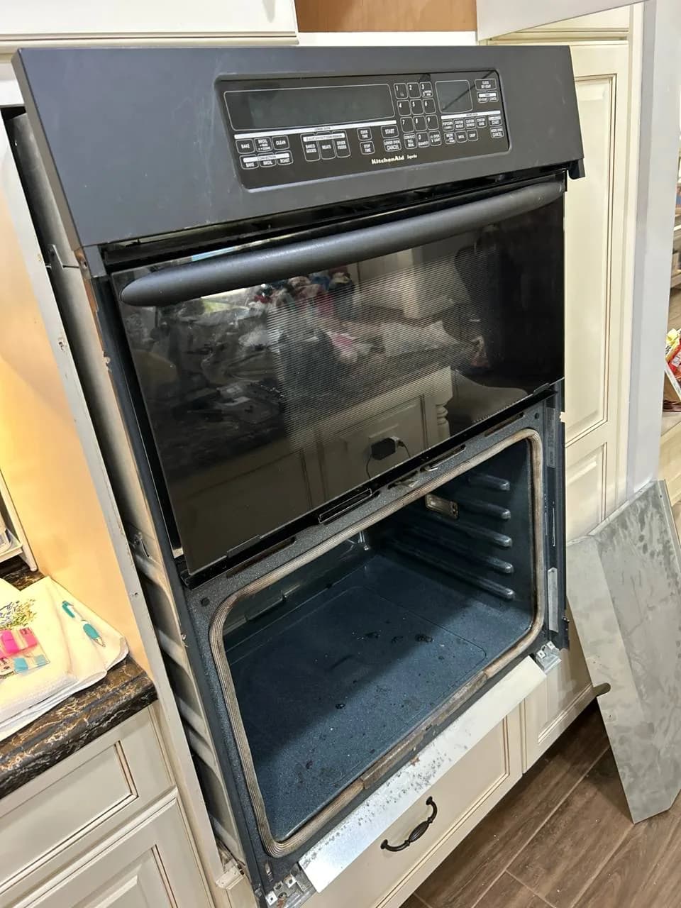 A built-in KitchenAid oven is pulled out of its cabinet for repair, with its door open and an interior panel removed