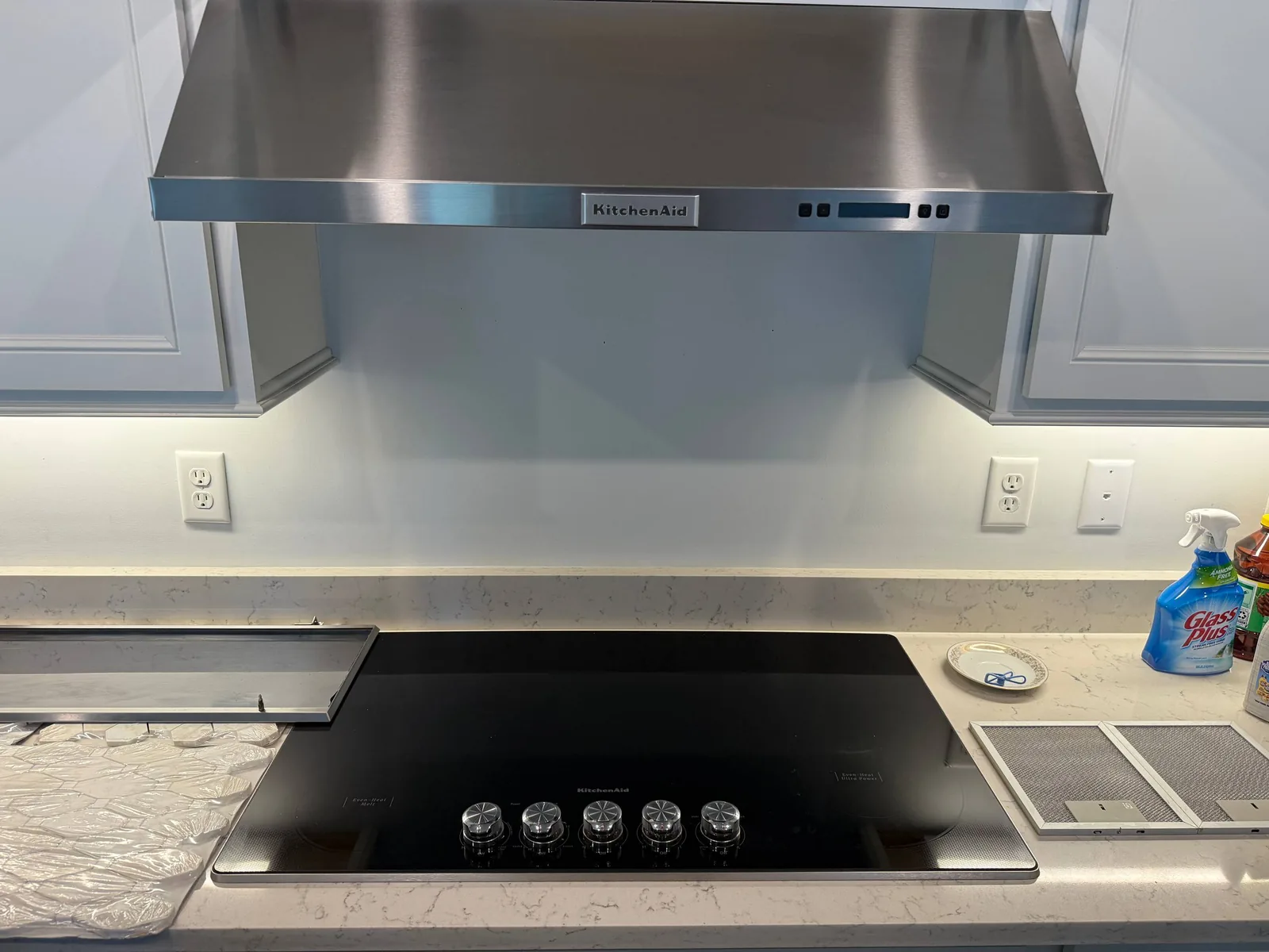 A new KitchenAid cooktop and range hood are installed in a kitchen with white cabinets