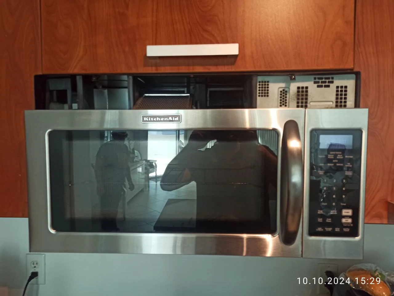 A stainless steel KitchenAid microwave with the top panel open, reflecting a technician in the door