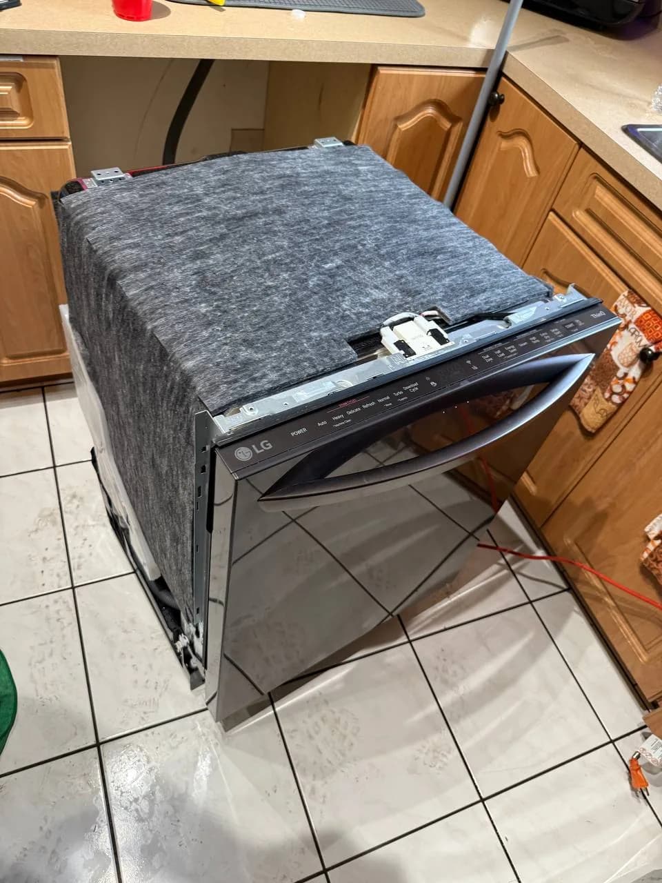 A new LG dishwasher on a tiled floor, unwrapped and ready for installation next to kitchen cabinets