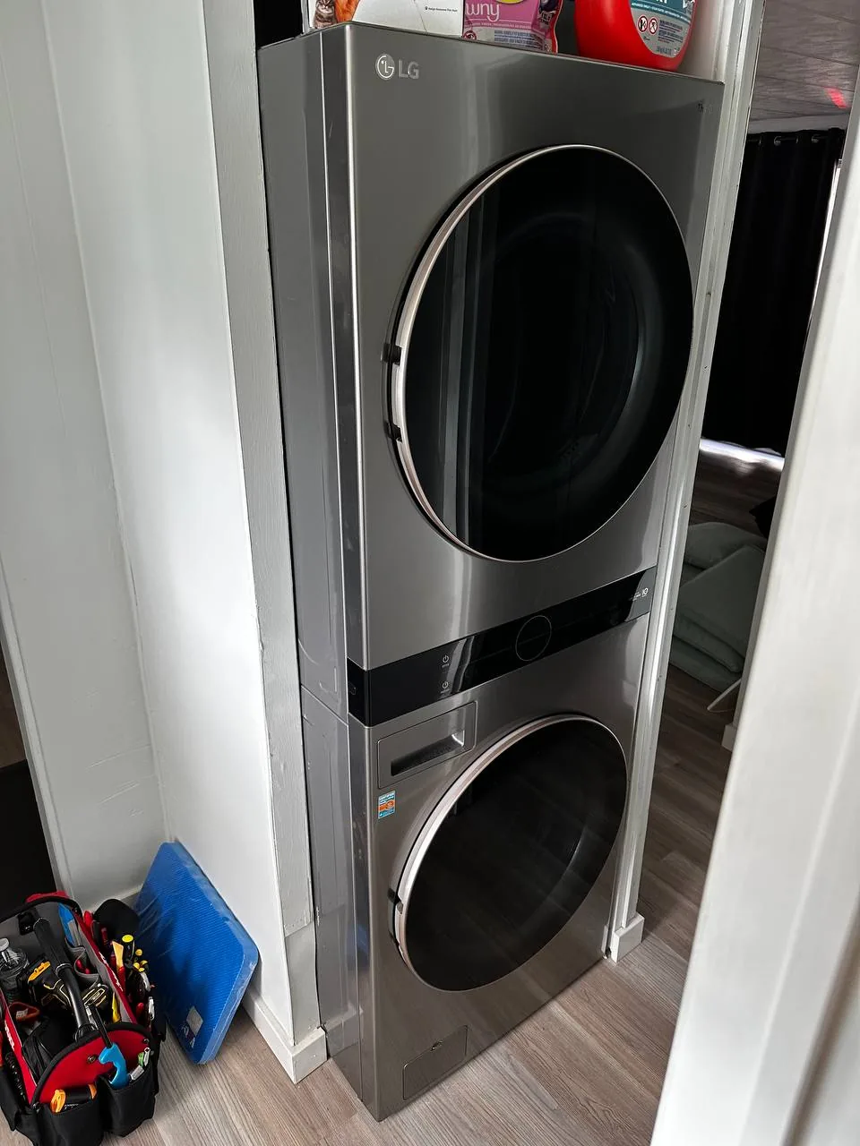 A modern LG washer and dryer combo unit in a small laundry area with a tool bag nearby
