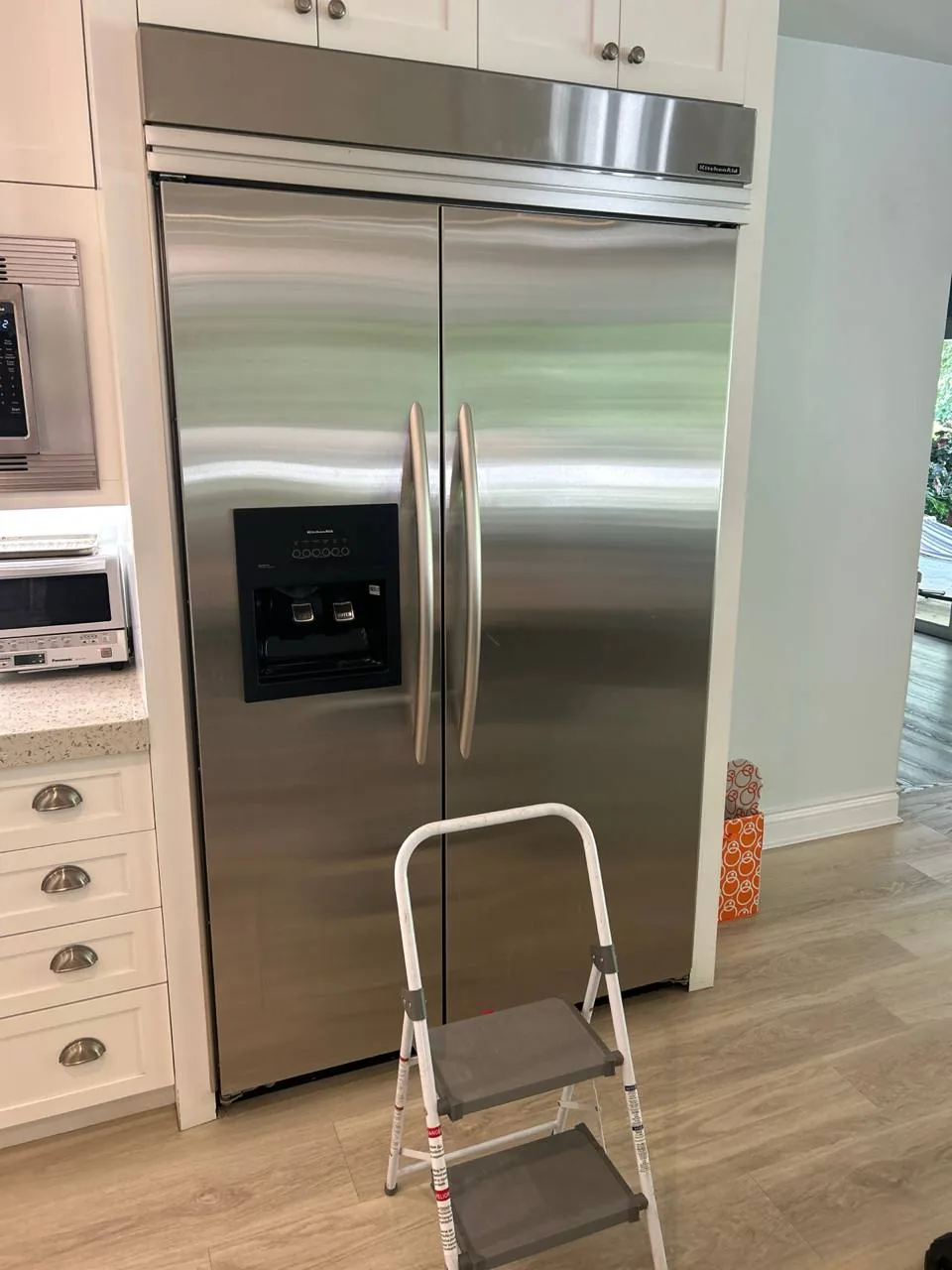 A stainless steel side-by-side refrigerator with a water and ice dispenser in a kitchen setting with a step stool in front
