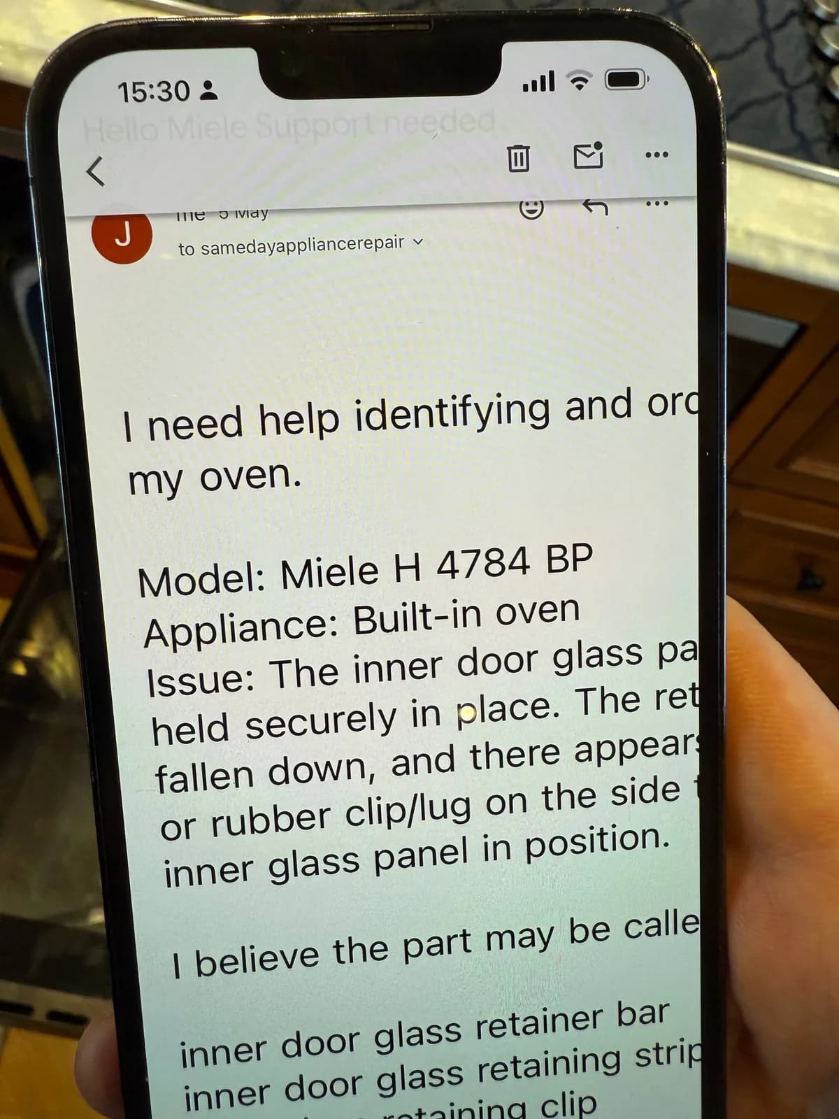 A person is holding a phone displaying an email about a Miele built-in oven repair issue