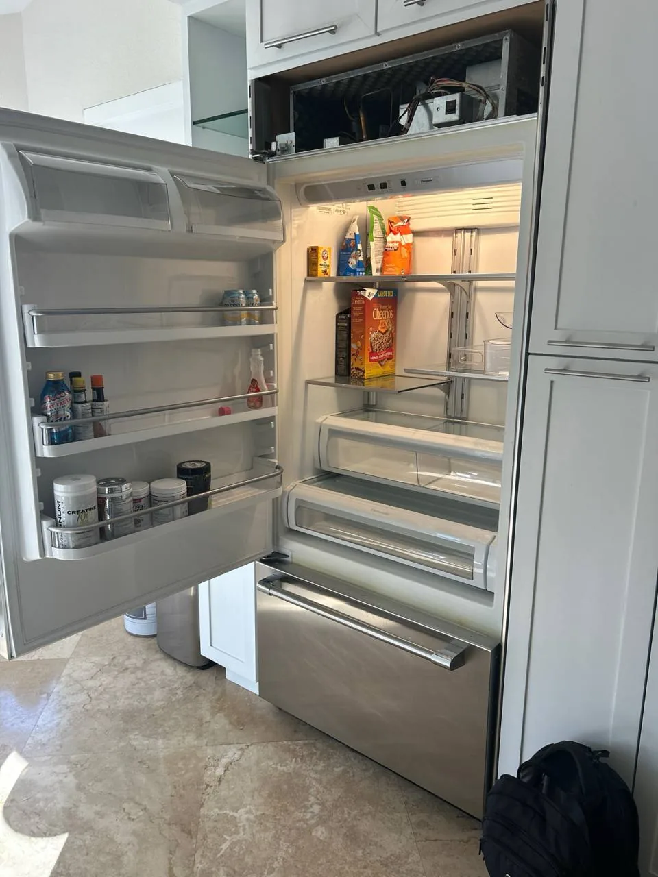 A stainless steel refrigerator with its top door open, revealing the interior shelves and some food items, along with the
