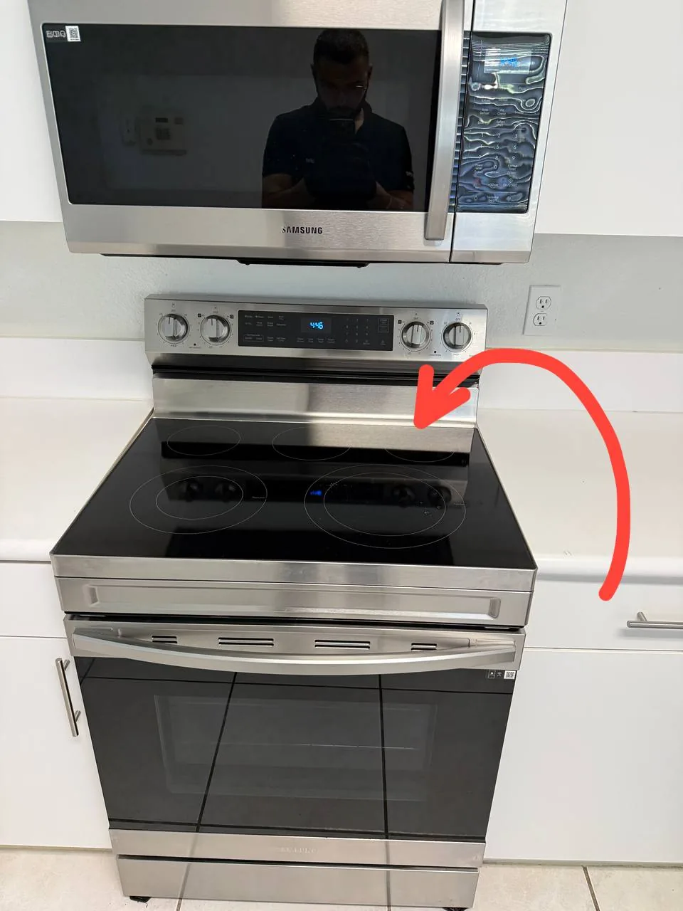 A stainless steel Samsung oven and microwave, with a technician's reflection in the microwave door