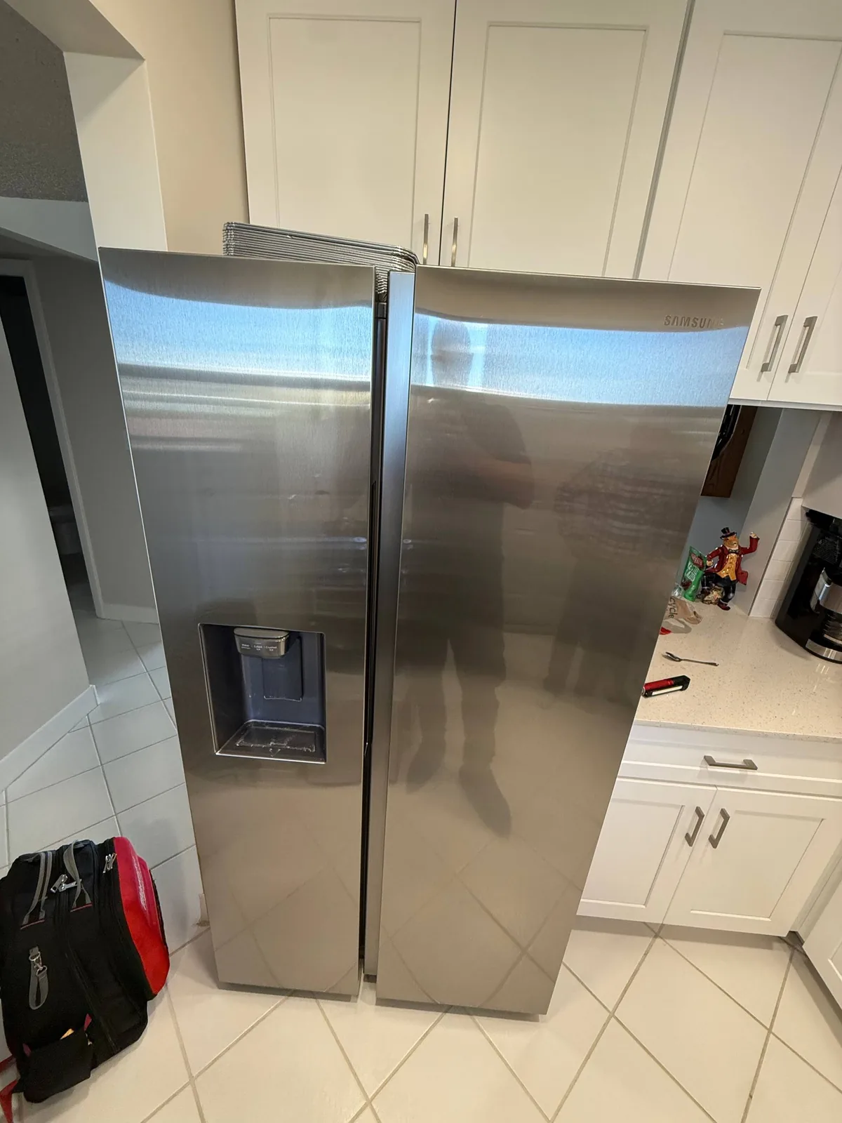 A stainless steel Samsung refrigerator in a kitchen with a reflection of a technician