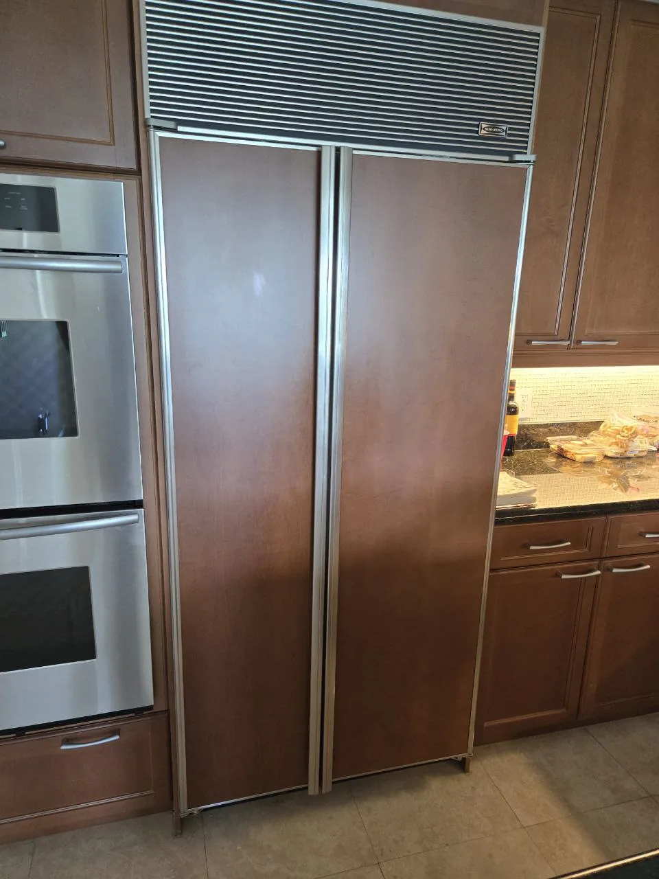 A Sub-Zero built-in refrigerator with custom wood panels and a stainless steel oven in a kitchen