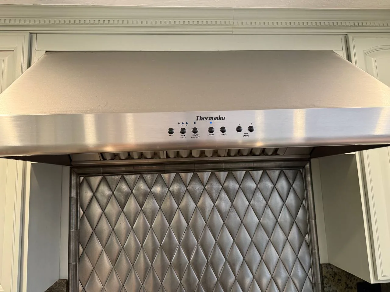 A stainless steel Thermador range hood installed above a backsplash
