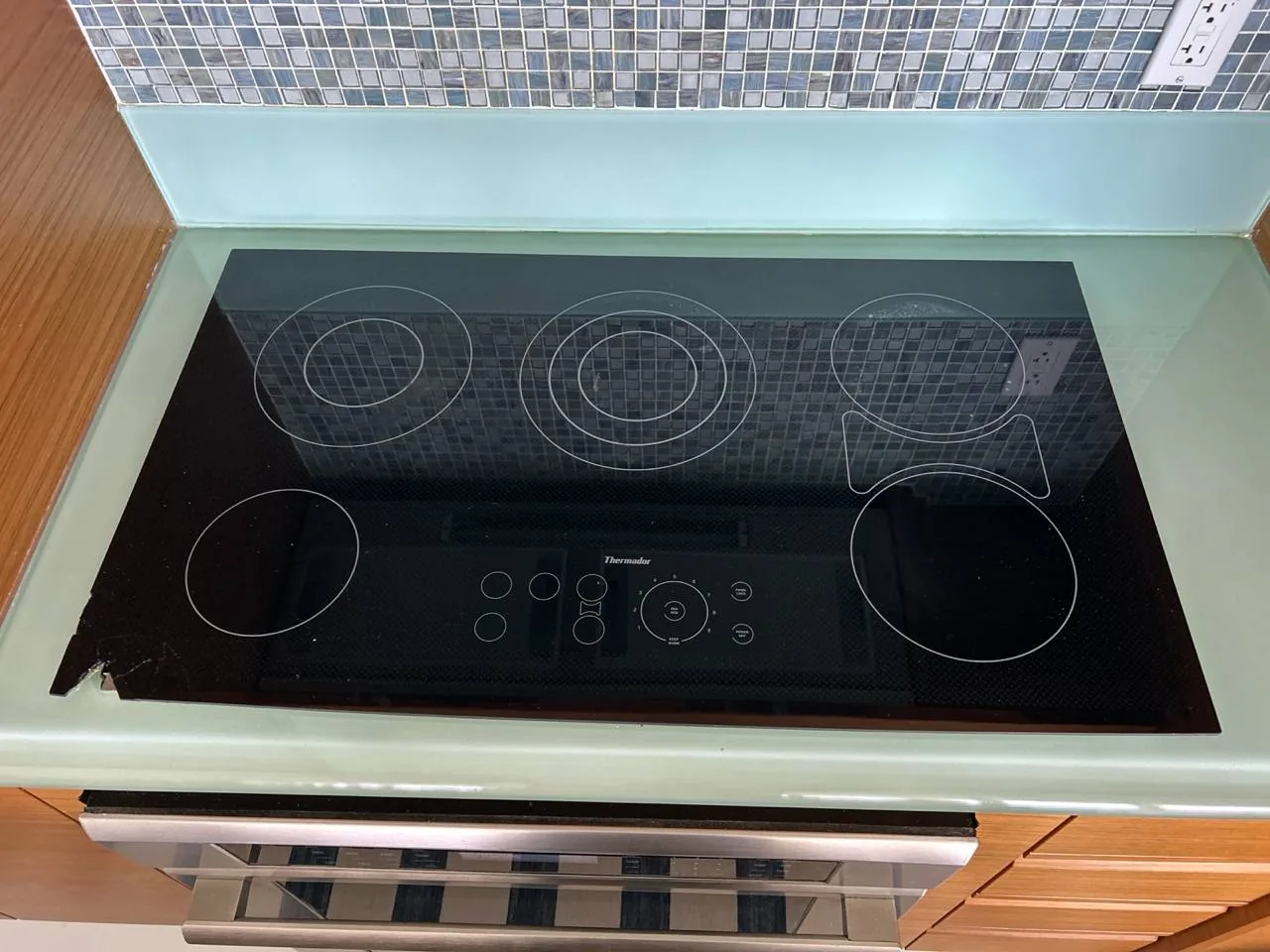 A Thermador electric cooktop with a chipped corner in a kitchen setting with a tiled backsplash