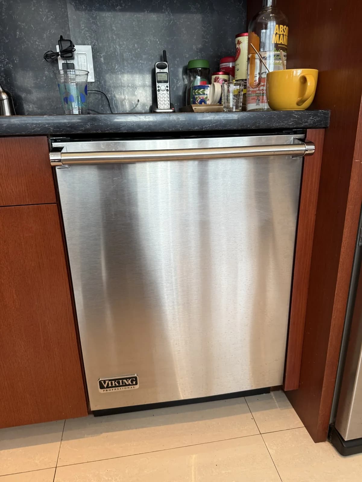 A stainless steel Viking dishwasher installed in a kitchen with wooden cabinets and a dark countertop