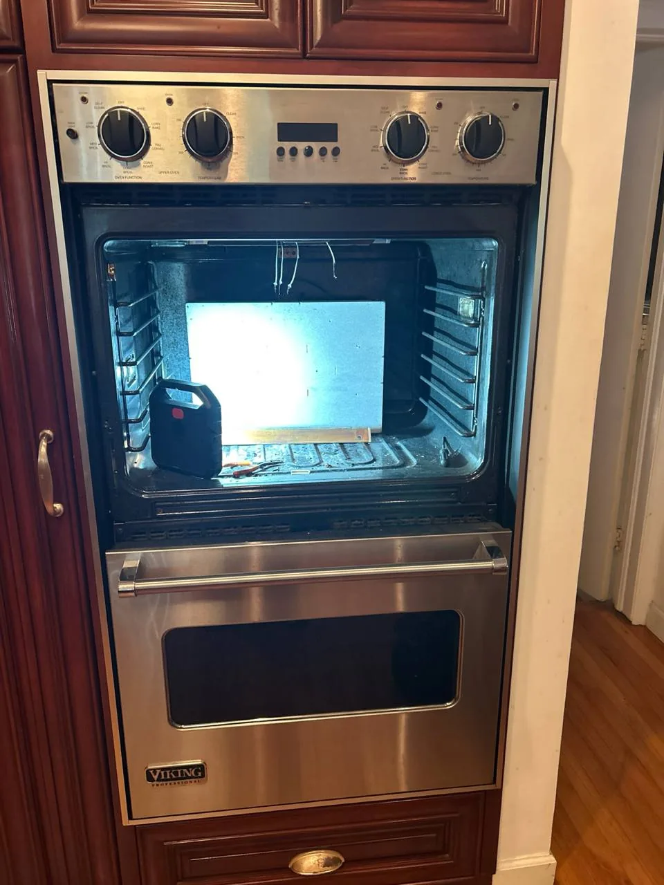 A Viking wall oven with its door open, revealing tools inside and a light illuminating the interior