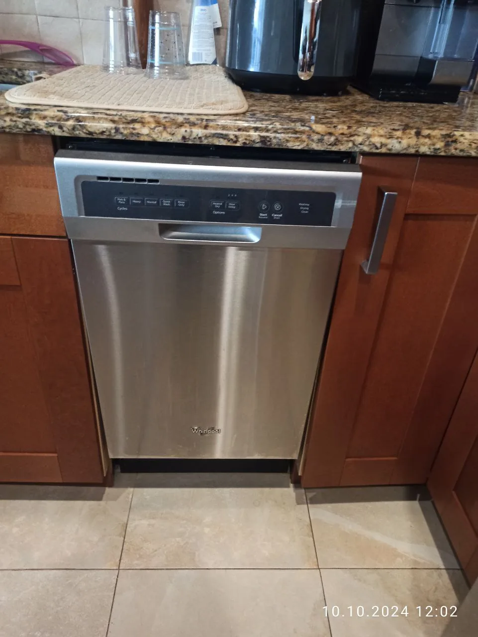 A stainless steel Whirlpool dishwasher installed under a granite countertop