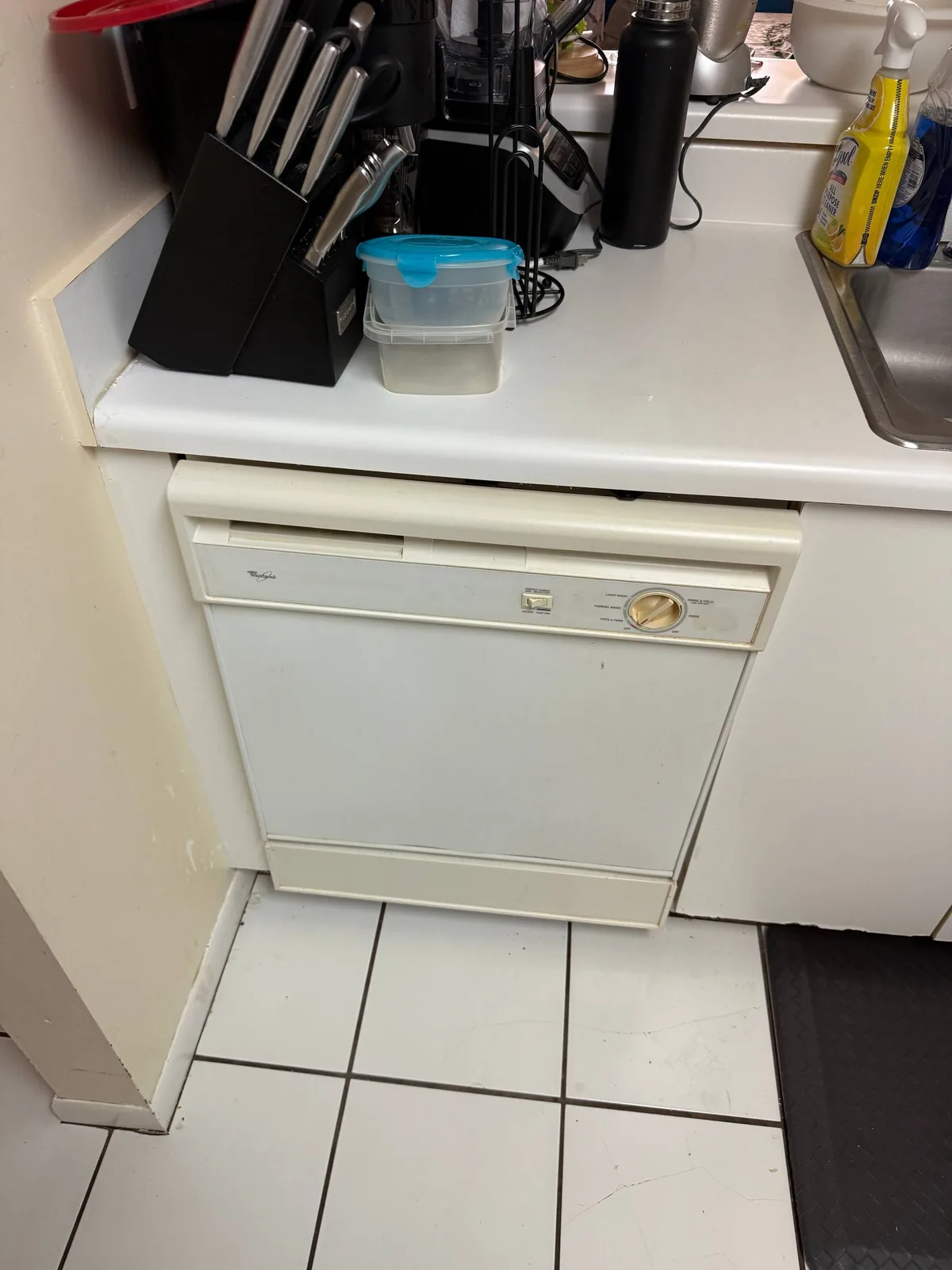 A white Whirlpool dishwasher is installed under a kitchen counter next to a sink
