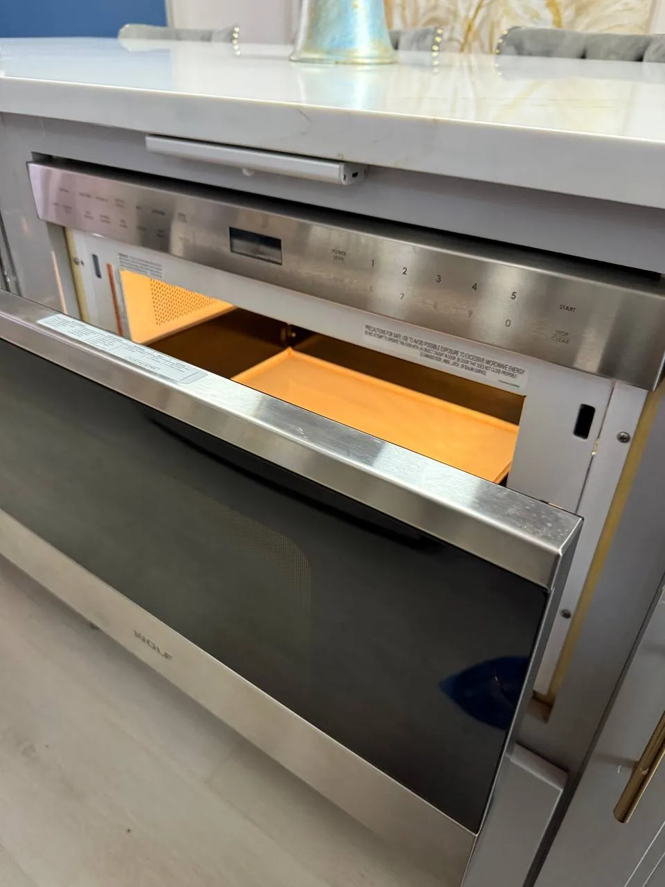 A stainless steel Wolf microwave with its drawer door open, showing the interior and control panel